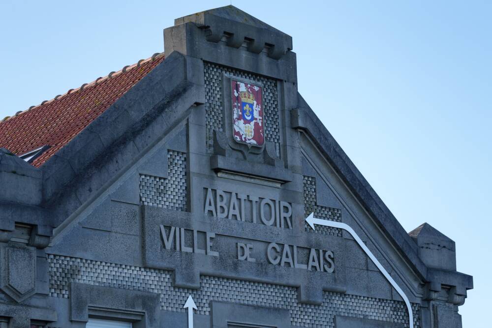 Vue avant de la façade du Channel, Scène Nationale à Calais arborant le blason de la ville et l'enseigne gravée des anciens abattoirs.