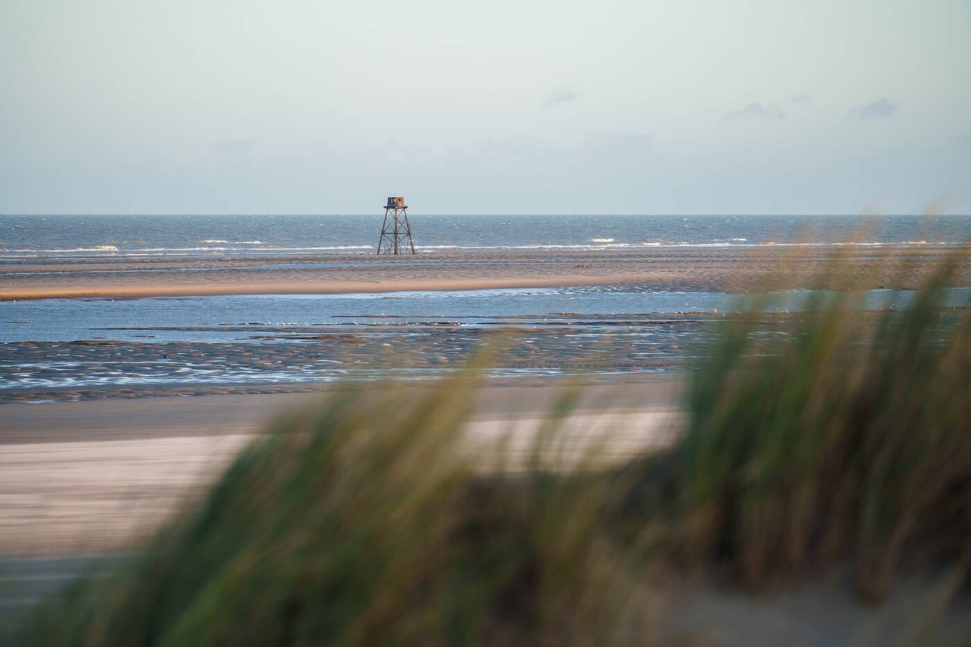 La plage préservée au premier plan cède la vue à la mer et le Phare de Walde qui marque la séparation entre Mer du Nord et la Manche.