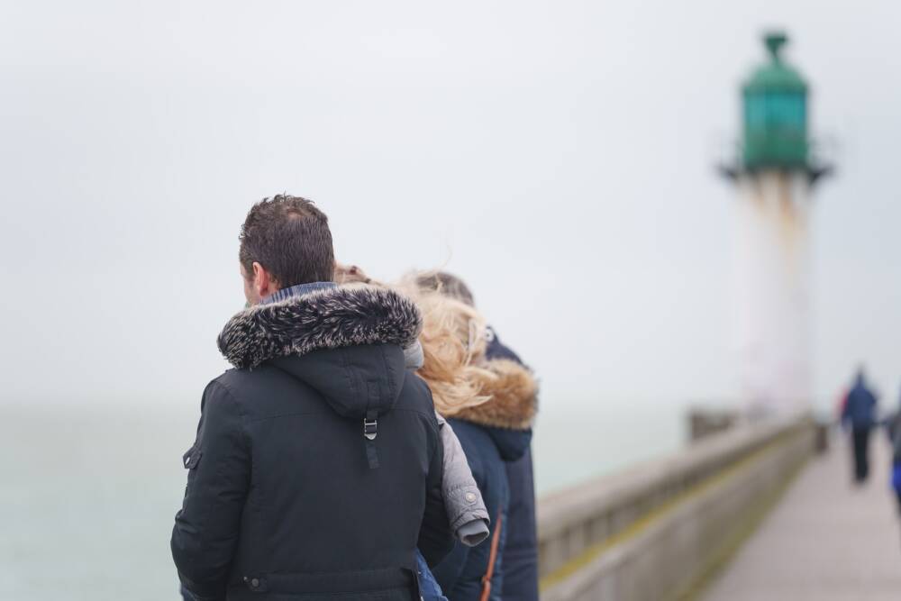 Une famille tournée vers la mer depuis la jetée de Calais avec le phare en arrière plan.