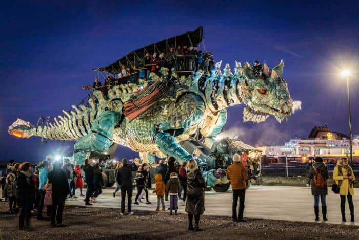 Dragon de Calais arpentant le front de mer de Calais sous un ciel nocturne d'hiver et les ferries défilant en arrière-plan.