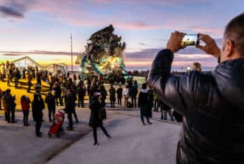 Le Dragon de Calais entouré de nombreux passants lors d'un coucher de soleil hivernal sur la plage de Calais.