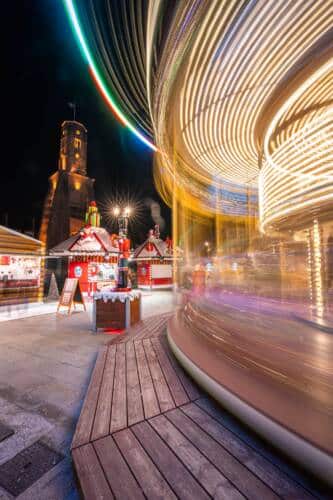 Vue du Carrousel 1900 de la Place d'Armes de Calais qui tournoie au pied de la Tour du Guet illuminée de nuit.