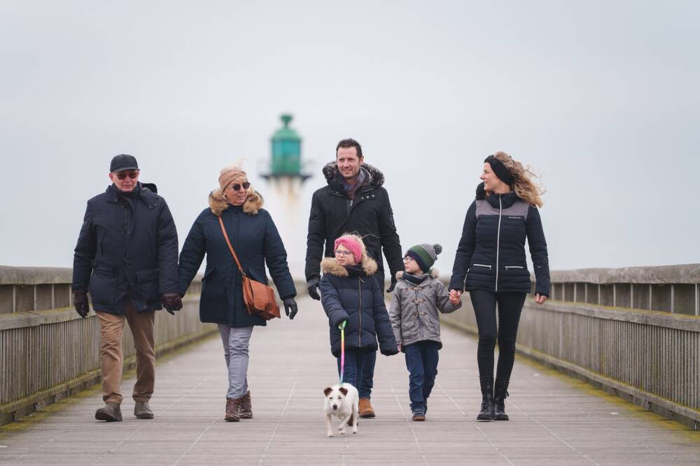 Une famille en promenade sur le jetée de Calais et son phare en arrière-plan.