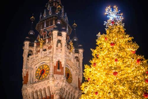 Le beffroi de Calais éclairé dans la nuit et les lueurs du sapin de Noël sur la Place du Soldat Inconnu