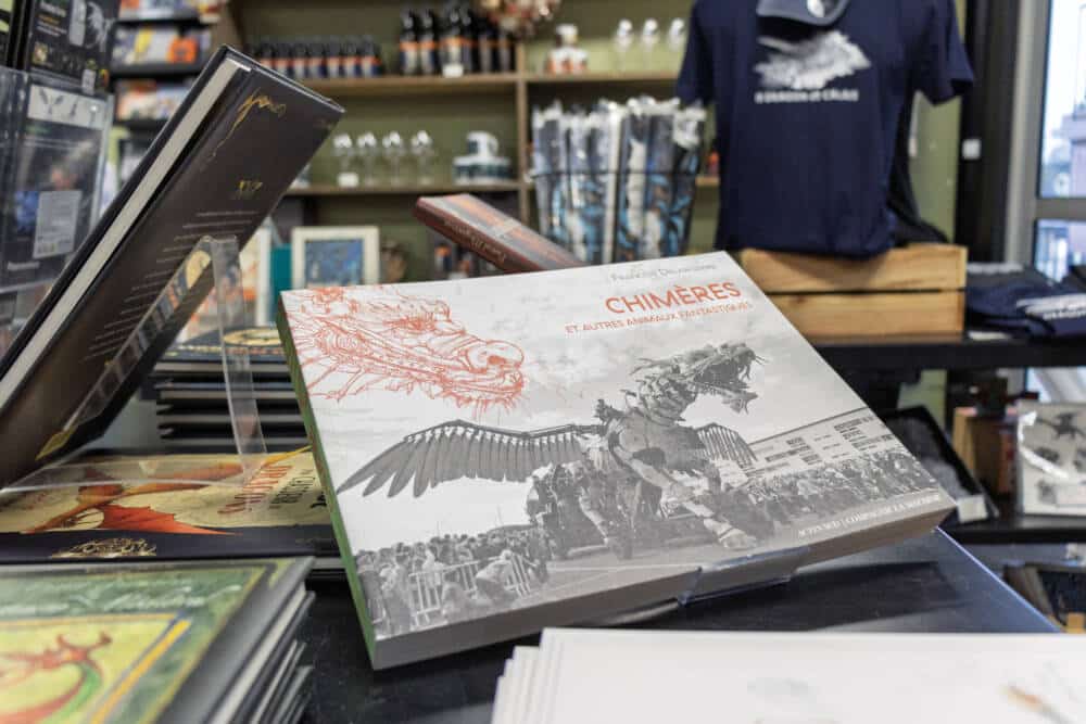 Chimères et autres animaux fantastiques” de François Delaroziere, en exposition dans la boutique de la Compagnie du Dragon à Calais. Couverture illustrée avec un croquis et une photo de Long Ma à Calais, entouré de produits dérivés et de souvenirs liés à l’univers de la compagnie.