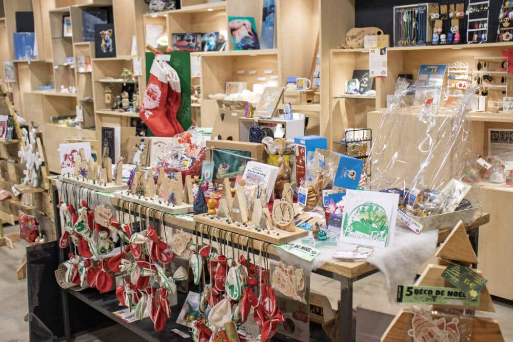 Vue d’ensemble de l’assortiment de Noël à la boutique du Comptoir de l’Îlot à Calais, mettant en avant des créations artisanales uniques. Décorations festives, cartes de vœux, chaussettes de Noël et objets en bois occupent les étals, dans une ambiance chaleureuse et créative.