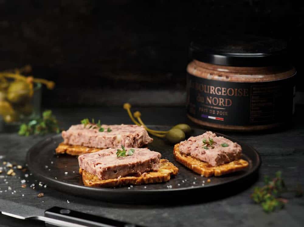 Terrine “La Bourgeoise du Nord” de la Maison Huchin à Coquelles, servie sur des toasts croustillants. Présentation gourmande avec câpres et herbes fraîches, reflétant la richesse du terroir culinaire des Hauts-de-France. Une spécialité locale parfaite pour les apéritifs festifs.