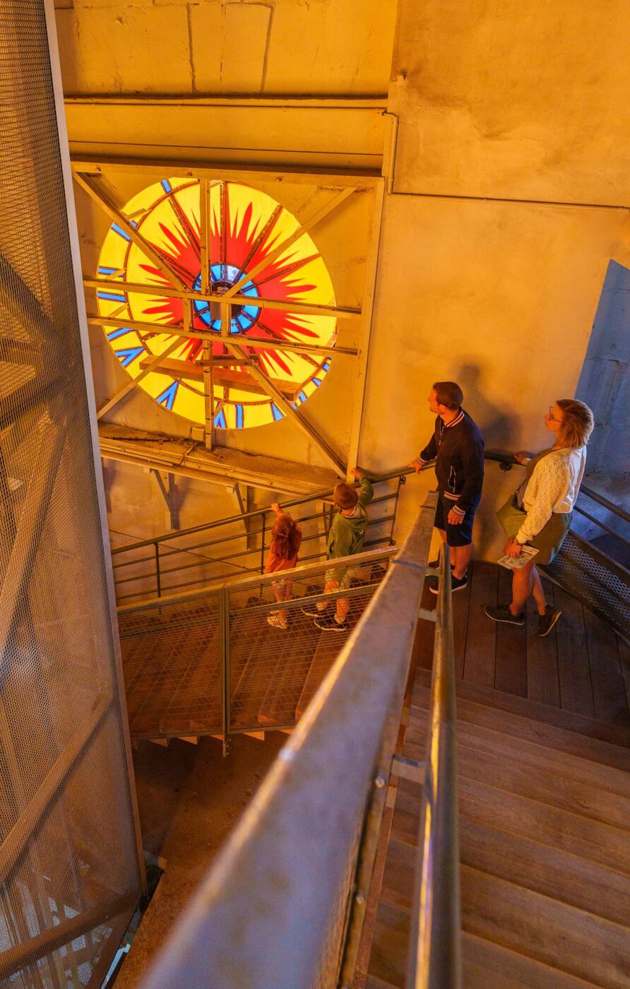 L’intérieur du beffroi de l’Hôtel de Ville de Calais, offrant une vue unique sur l’arrière du cadran de l’horloge, illuminé par la lumière extérieure.