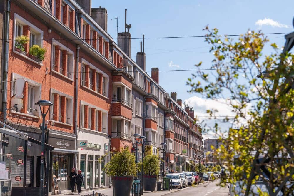 Vue ensoleillée de la rue Royale à Calais, bordée de commerces et de bâtiments en briques typiques de la reconstruction d’après-guerre. Cette artère commerçante dynamique relie le centre-ville au front de mer, offrant une ambiance chaleureuse et conviviale pour les habitants et visiteurs.