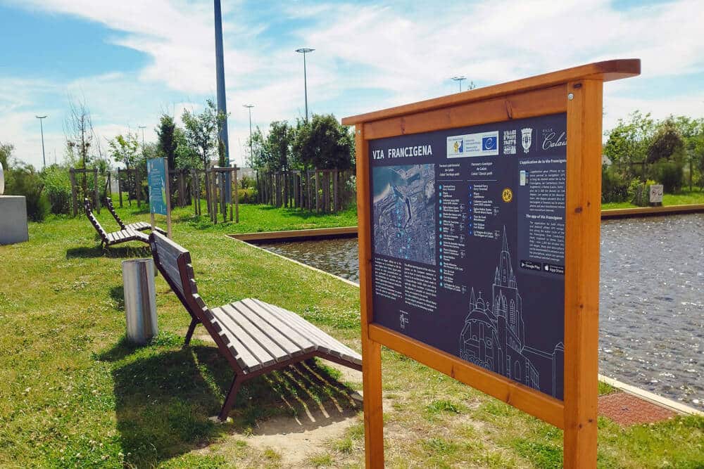 Signalétique en bois du parcours de la Via Francigena près du port de Calais, illustrant la route de pèlerinage européenne.